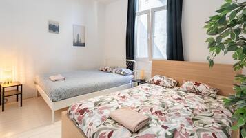 A bedroom with two beds, a bedside table with a lamp, a radiator, and a window with curtains.
