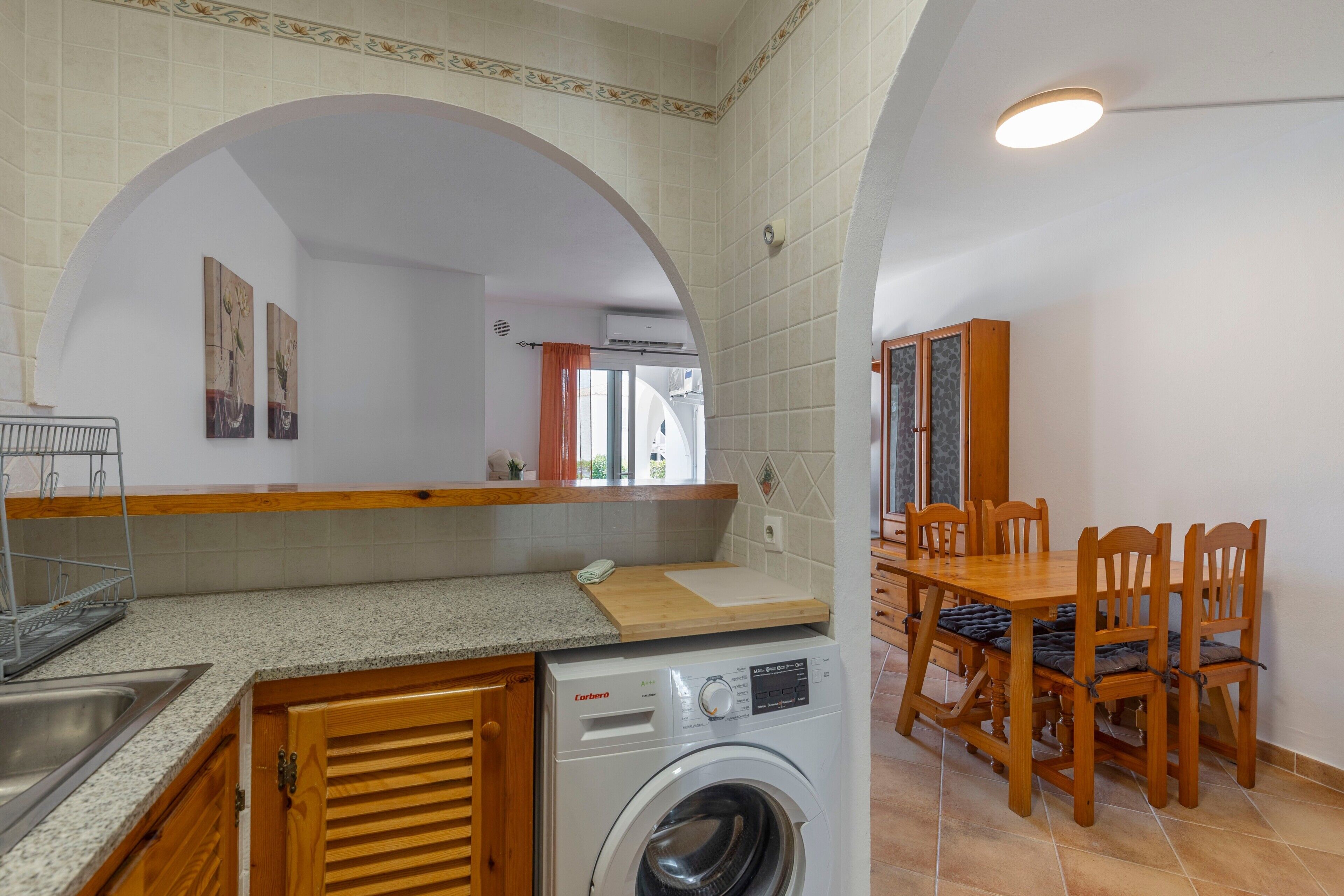 Cocina compacta con lavadora, mesa de comedor de madera y sillas.