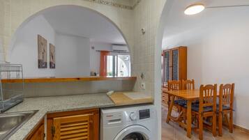 Cocina compacta con lavadora, mesa de comedor de madera y sillas.