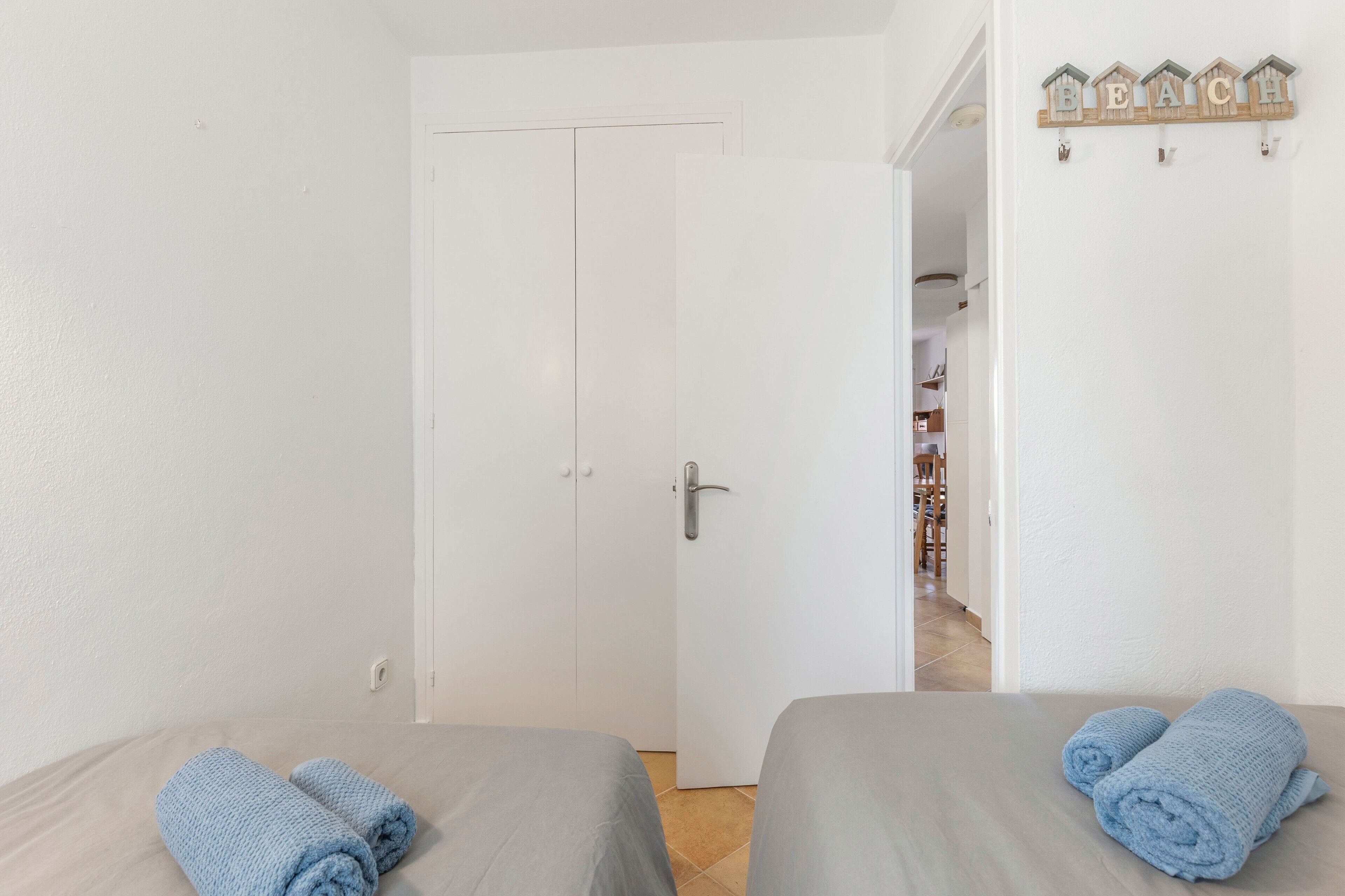 Una habitación con dos camas, una puerta blanca y un pasillo que lleva a un baño.