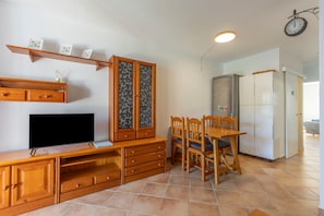 Una cocina compacta con una mesa de comedor, sillas, televisor, armarios de madera y un refrigerador.