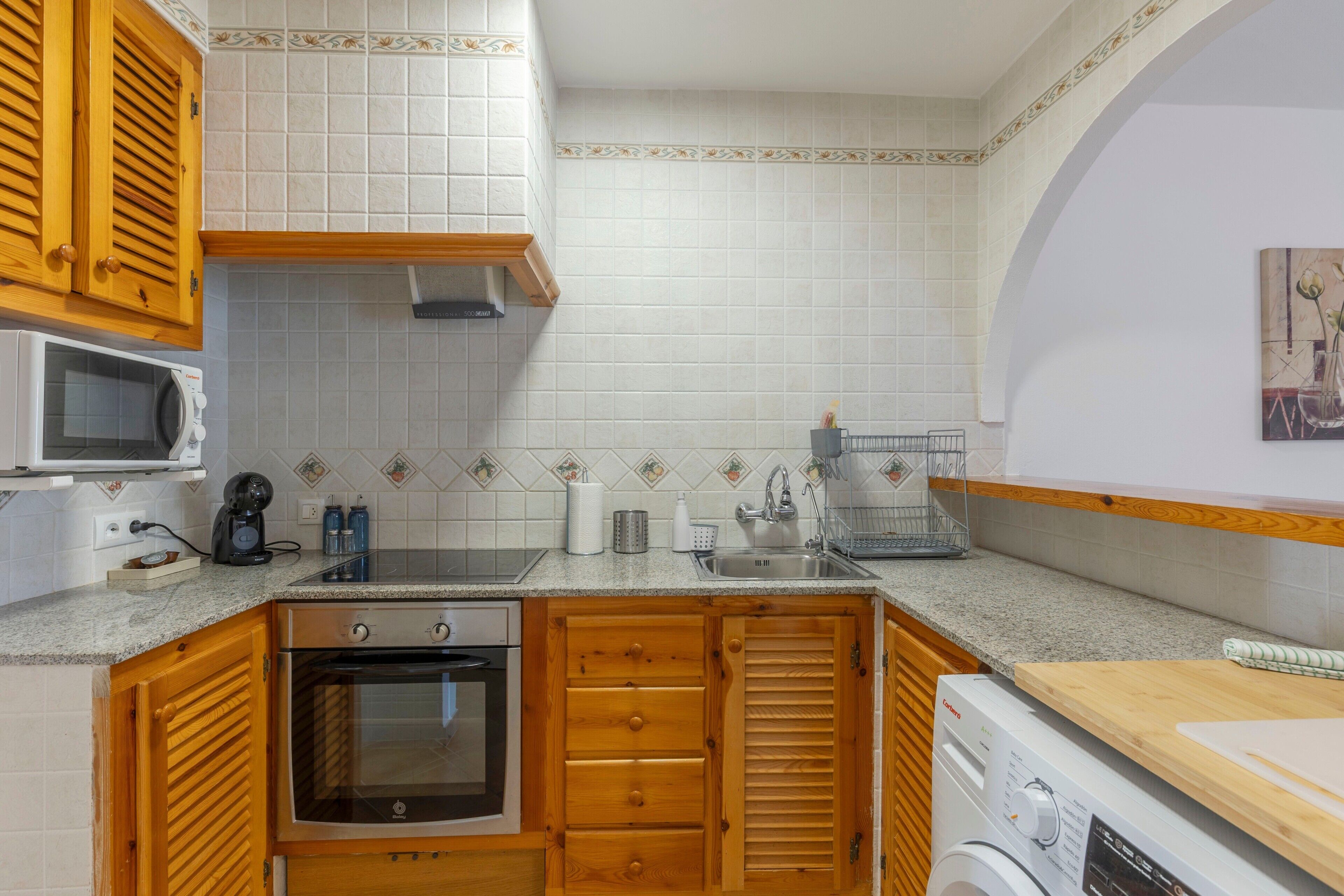 Una cocina compacta equipada con microondas, horno, armarios de madera, un lavabo y una lavadora.
