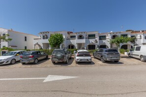 Un parcheggio con diverse auto parcheggiate di fronte a un edificio con numerosi balconi e finestre ad arco.