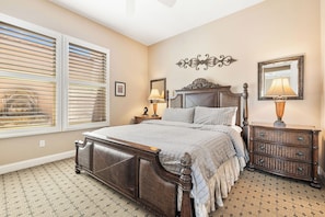 A bedroom with a large bed, a dresser, a nightstand, a wall-mounted mirror, and a window with blinds. - Veranda - On the Greg Norman Course at PGA! (La Quinta)