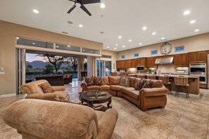 A spacious living room with a large L-shaped sectional sofa, a coffee table, and a dining area with bar stools. The kitchen features wooden cabinets and stainless steel appliances. - Veranda - On the Greg Norman Course at PGA! (La Quinta)