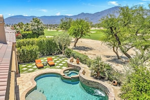A swimming pool with a stone border, two lounge chairs, and a view of a golf course and mountains. - Veranda - On the Greg Norman Course at PGA! (La Quinta)