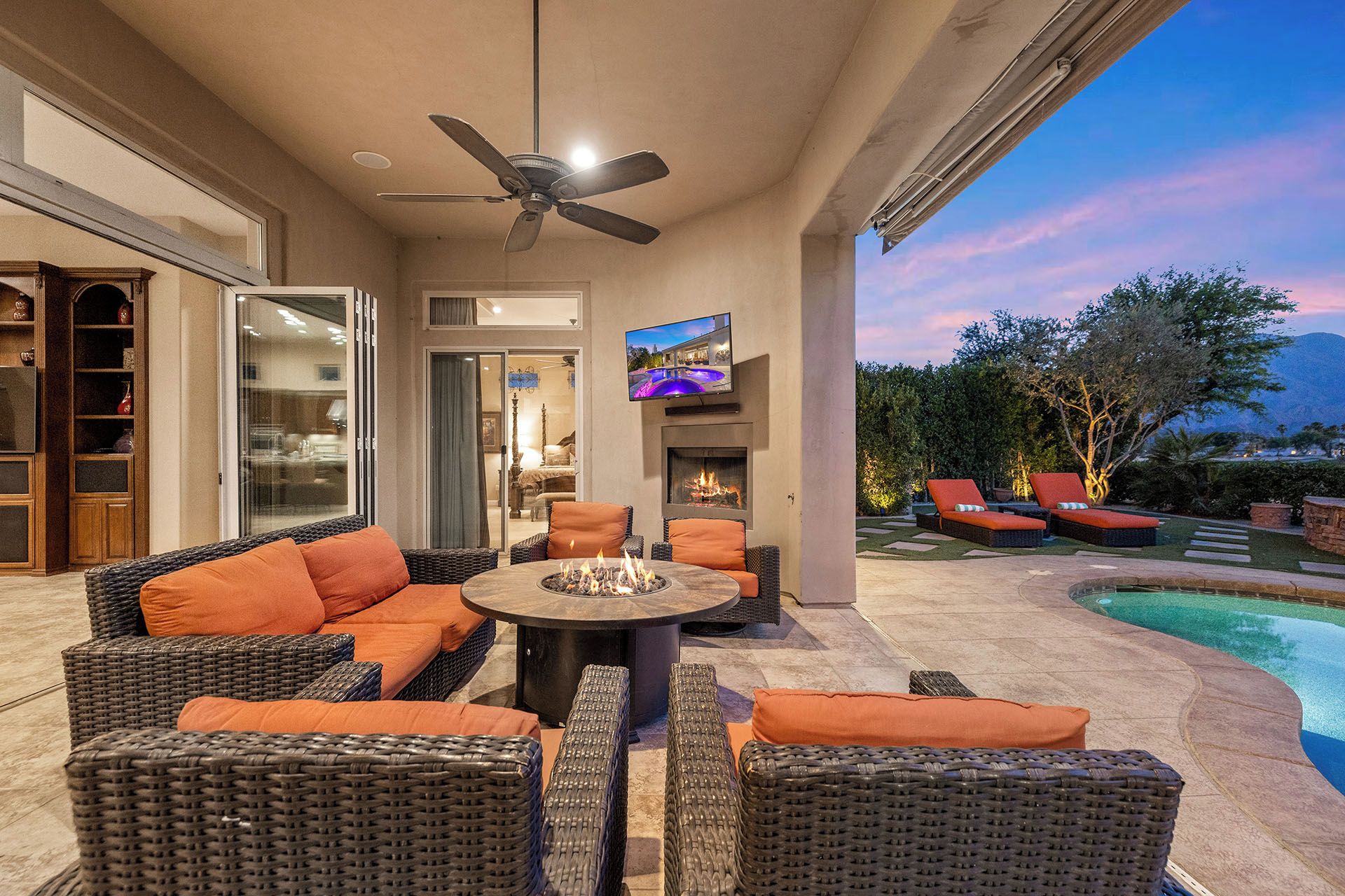 An outdoor patio with wicker furniture, a ceiling fan, a TV, and a pool.