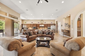 A spacious living room with a large L-shaped sectional sofa, a coffee table, and a kitchen in the background. - Veranda - On the Greg Norman Course at PGA! (La Quinta)