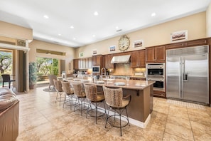 A spacious kitchen with a central island, stainless steel appliances, and a dining area with wicker chairs. - Veranda - On the Greg Norman Course at PGA! (La Quinta)