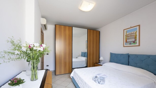 Un dormitorio con cama, mesita de noche, espejo y un cuadro colgado en la pared.
