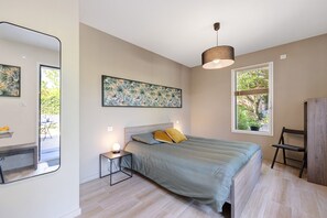 Ein Schlafzimmer mit Bett, Nachttisch, Lampe, Kunstwerk, Fenster und Spiegel.