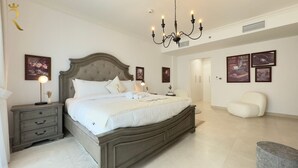 Quarto com uma cama grande, mesas de cabeceira, um candelabro e quadros nas paredes.