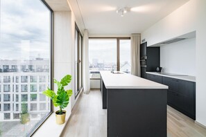 Eine moderne Küche mit einer großen Kochinsel, dunklen Schränken und Blick auf die Stadt durch große Fenster.