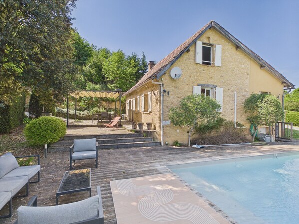 A stone house with a swimming pool, outdoor seating, and a covered patio area.