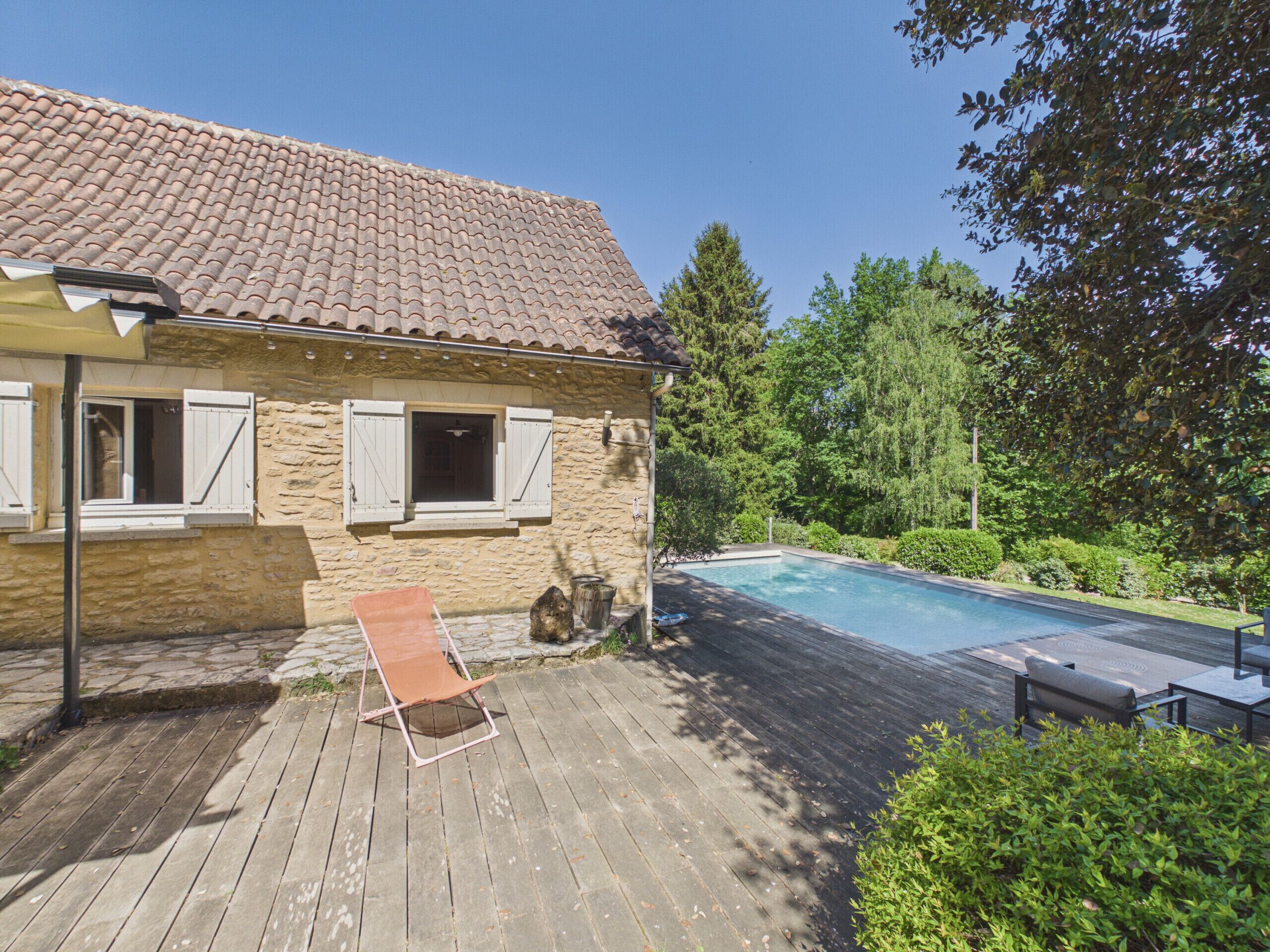 A house with a tiled roof, a swimming pool, a wooden deck, and a garden.