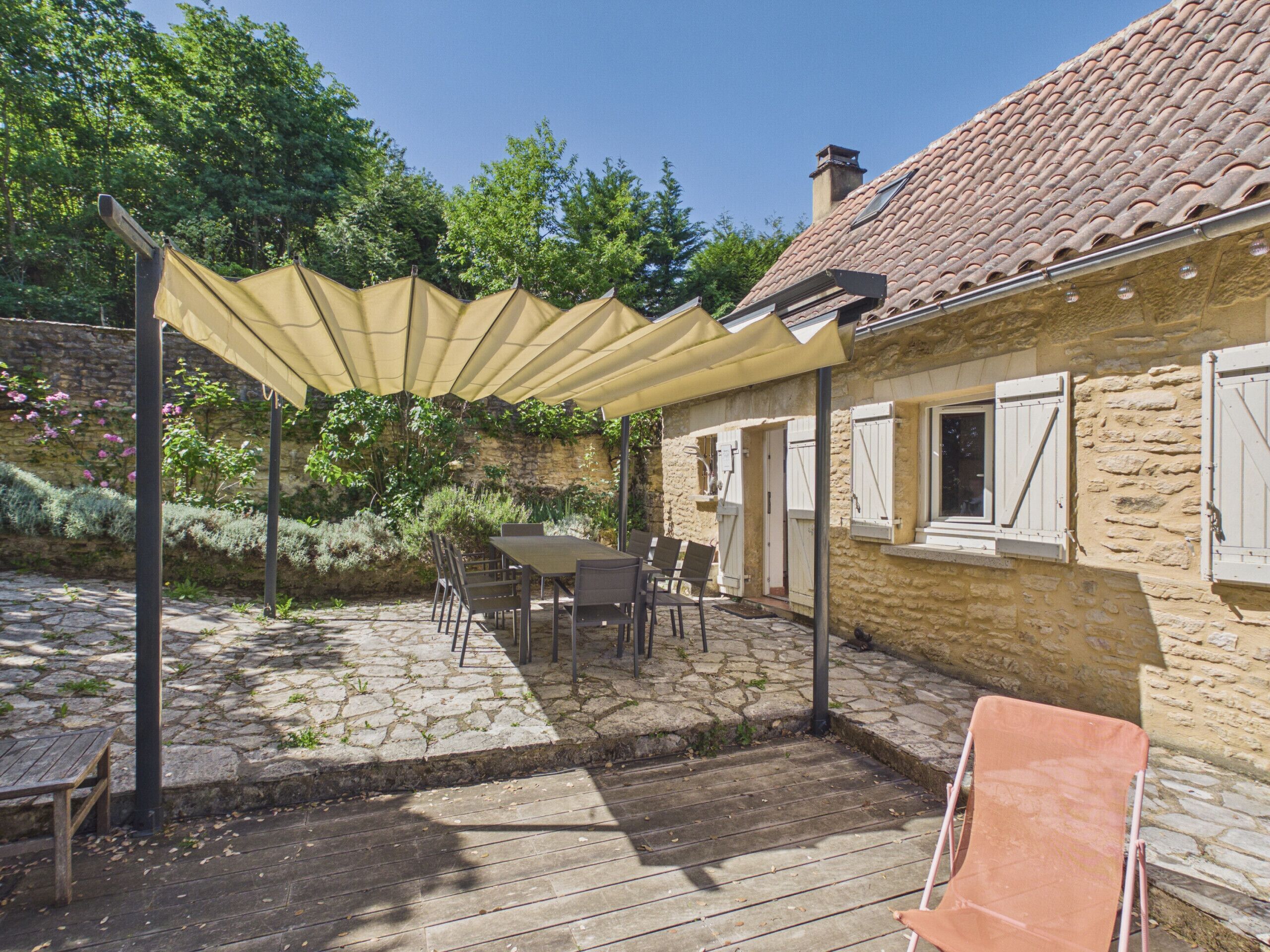 A stone patio with a table and chairs, a covered seating area, and a stone wall with vegetation.