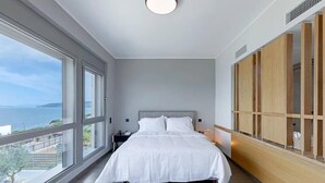 A bedroom with a large window, a bed, a nightstand, and a wooden wardrobe.