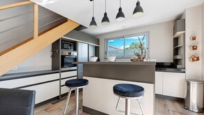 A modern kitchen with a central island, bar stools, and a staircase. - Holiday Home "Maison Vent d’Ouest" with Private Terrace and Wi-Fi in La Tranche sur Mer (La Tranche-sur-Mer)