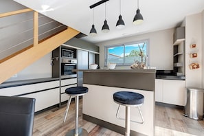 A modern kitchen with a central island, bar stools, and a staircase. - Holiday Home "Maison Vent d’Ouest" with Private Terrace and Wi-Fi in La Tranche sur Mer (La Tranche-sur-Mer)