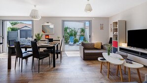 A modern living room with a dining area, a sofa, a TV, and a large window. - Holiday Home "Maison Vent d’Ouest" with Private Terrace and Wi-Fi in La Tranche sur Mer (La Tranche-sur-Mer)