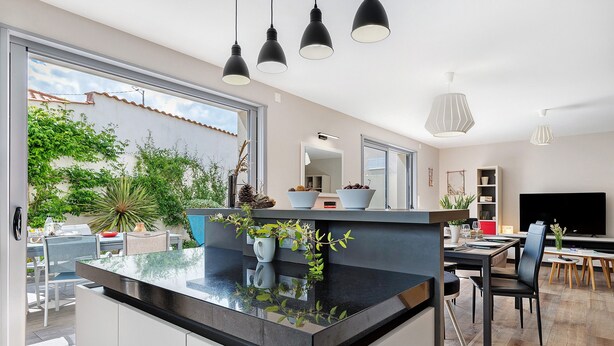 A modern kitchen with a black countertop, white cabinets, and a dining area with a TV and seating. - Holiday Home "Maison Vent d’Ouest" with Private Terrace and Wi-Fi in La Tranche sur Mer (La Tranche-sur-Mer)
