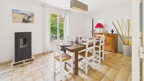 Un comedor con una mesa dispuesta para cuatro, una chimenea, un ventanal con cortinas y un cuadro en la pared.