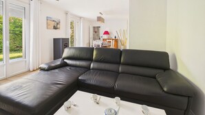 Una sala de estar moderna con un sofá seccional de cuero negro, una mesa de centro blanca con juego de té, y vistas al exterior a través de amplios ventanales.