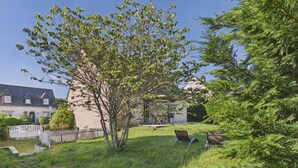 Un espacio verde con un árbol, un banco y un edificio de techo inclinado.