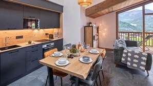 Una cucina moderna con mobili scuri, un tavolo da pranzo in legno apparecchiato per quattro persone e un balcone con vista sulle montagne.
