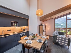 Eine moderne Küche mit dunklen Schränken, einem Holzespeisetisch für vier Personen und einem Balkon mit Bergblick.