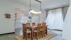 Et moderne spiseområde med et træbord og stole, en hængende lampe samt et køkken i baggrunden.
