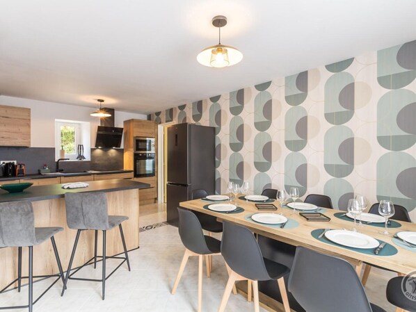 A modern kitchen with a central island, bar stools, a dining table set for six, and a patterned wall.