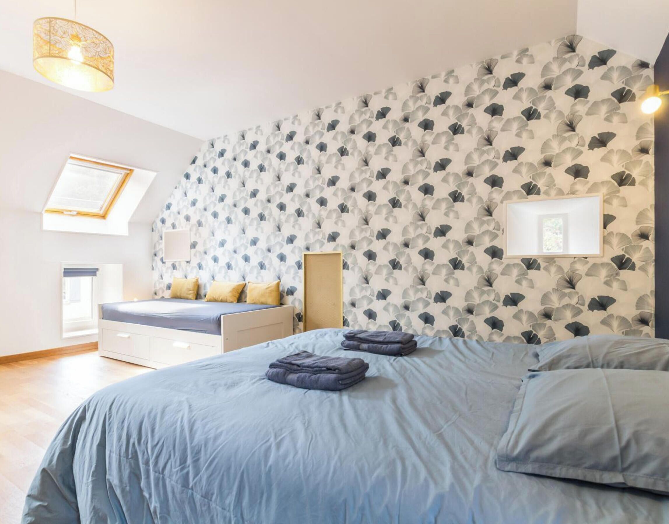 A bedroom with a bed, bedside tables, a bench, and a wall with a leaf pattern.