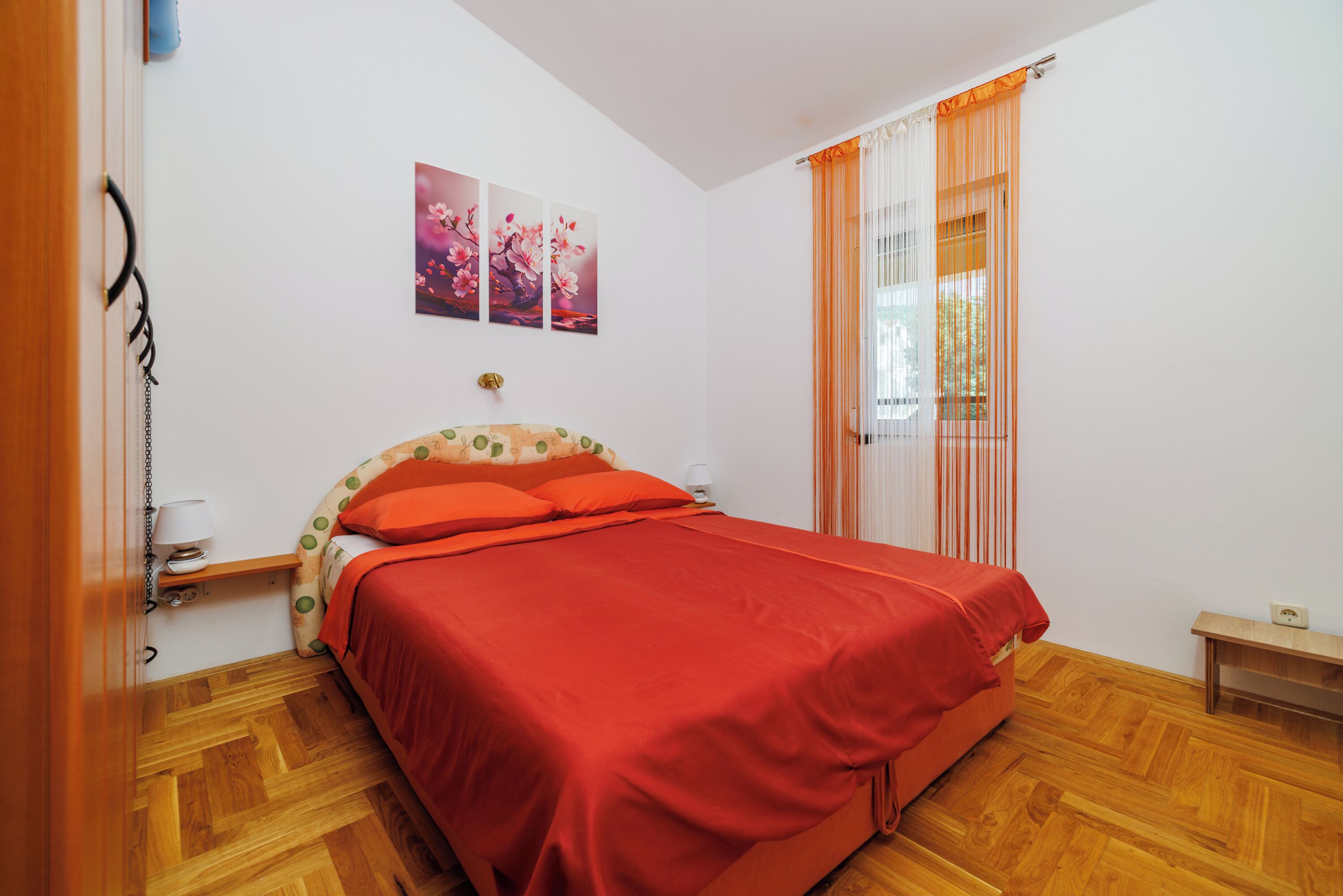 Un dormitorio con una cama, una mesita de noche, una lámpara y una ventana con cortinas.