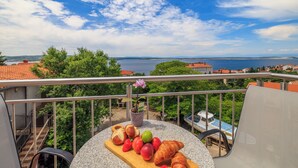 A balcony with a table set with fruits and a croissant, overlooking a body of water and greenery. - Apartment with fantastic sea view and balcony in Crikvenica (Crikvenica)