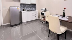 A modern kitchen with white cabinets, a refrigerator, a microwave, and a dining area with a table and chairs. - Luxurious 1-bedroom Condo With Pool Near Jomtien Beach (Pattaya)