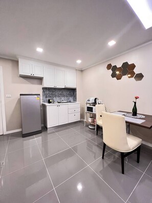 A modern kitchen with white cabinets, a refrigerator, a microwave, and a dining area with a table and chairs. - Luxurious 1-bedroom Condo With Pool Near Jomtien Beach (Pattaya)