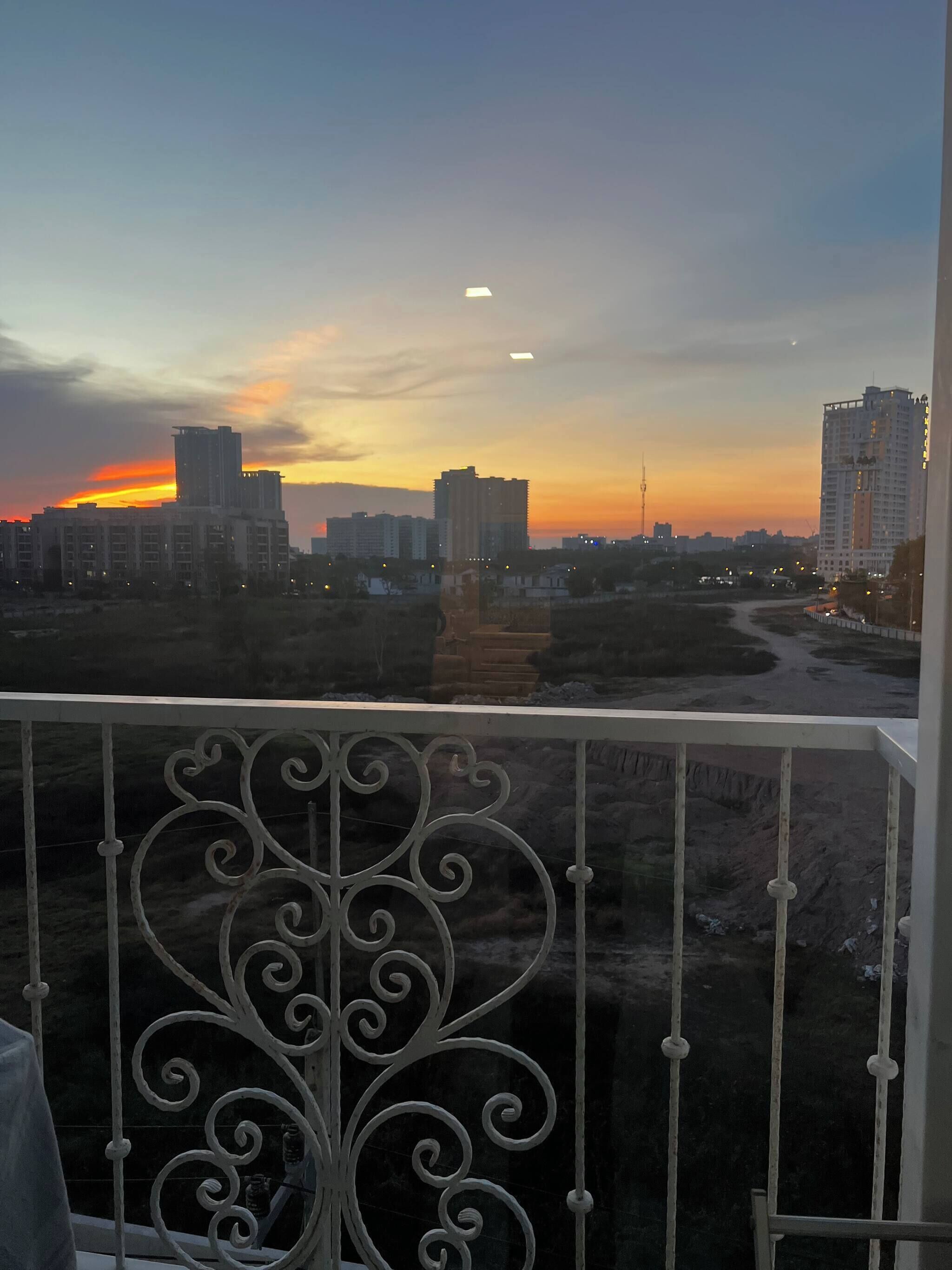 A balcony with ornate metal railings overlooking a cityscape during sunset.