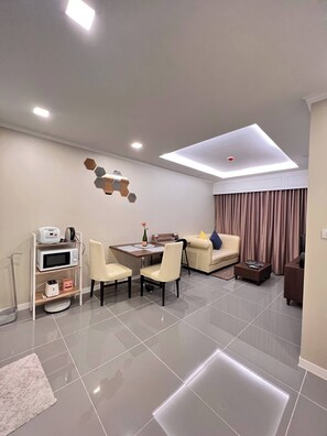 A modern living room with a dining area, a sofa, a coffee table, a TV, and a ceiling light fixture. - Luxurious 1-bedroom Condo With Pool Near Jomtien Beach (Pattaya)