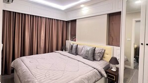 A modern bedroom with a large bed, a ceiling light, a wardrobe, and a mirror. - Luxurious 1-bedroom Condo With Pool Near Jomtien Beach (Pattaya)