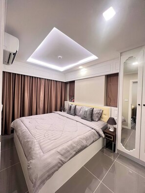 A modern bedroom with a large bed, a ceiling light, a wardrobe, and a mirror. - Luxurious 1-bedroom Condo With Pool Near Jomtien Beach (Pattaya)