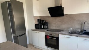 Eine moderne Küche mit einem Edelstahlkühlschrank, einer Mikrowelle, einer Kaffeemaschine, einem Gasherd und einem Spülbecken mit Geschirrgestell.