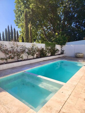 Una piscina rettangolare con acqua cristallina, circondata da un muro bianco e da una fila di alberi.