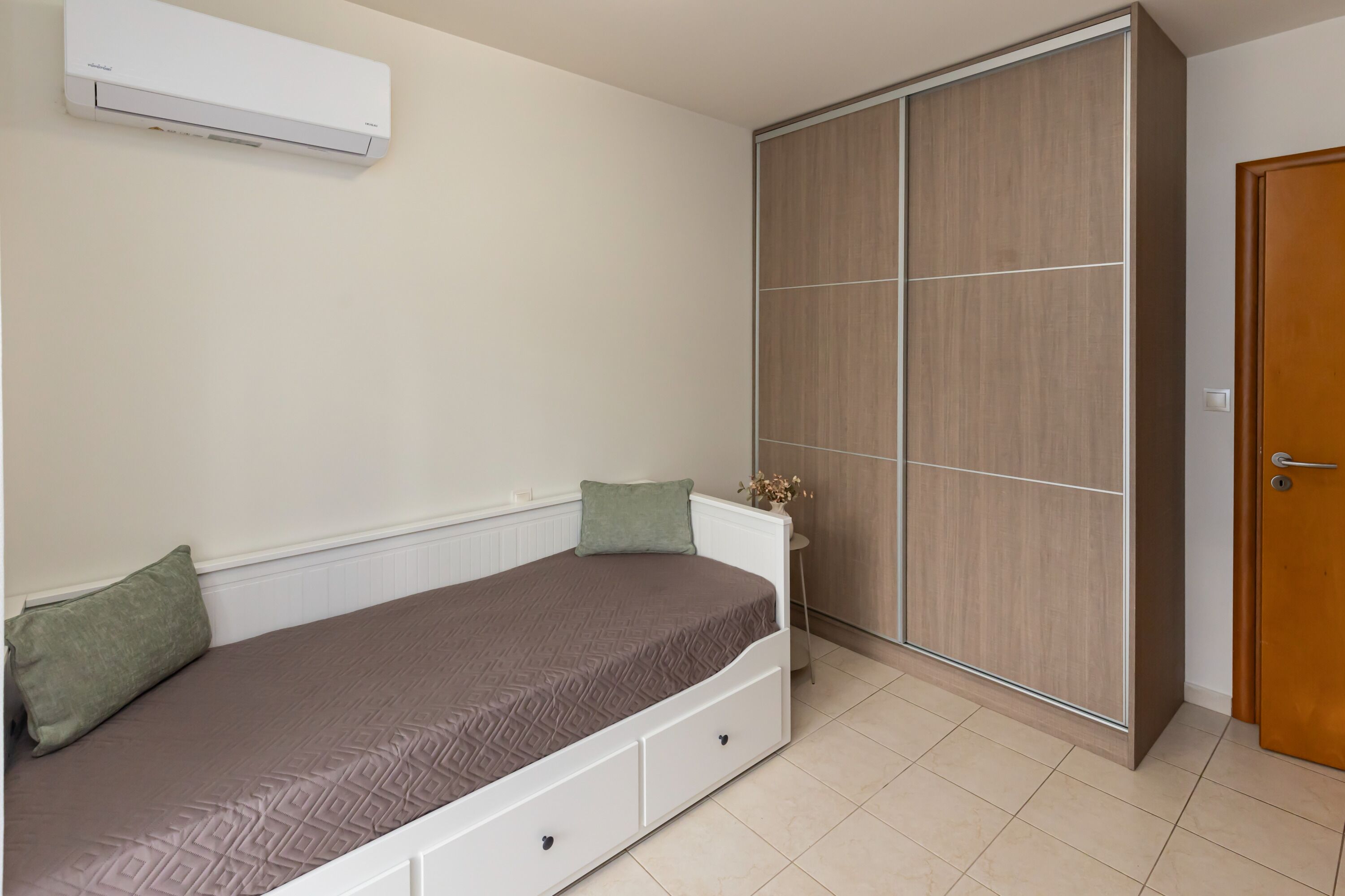 Un dormitorio con cama, armario, puerta y unidad de aire acondicionado.