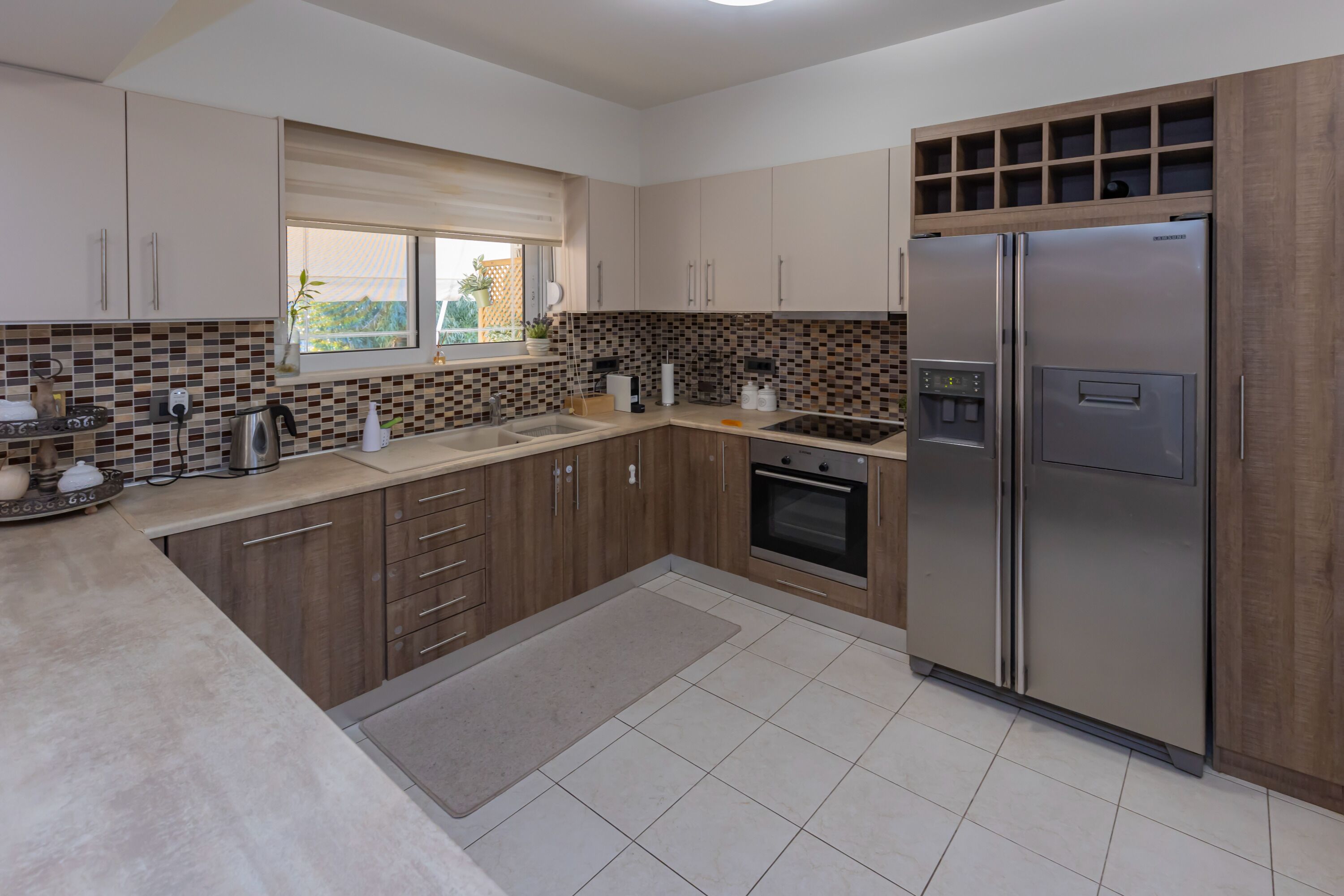 A modern kitchen with wooden cabinets, a built-in oven, a stainless steel refrigerator, and a window with a view.