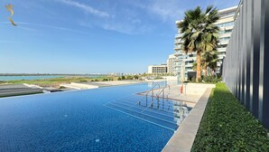 A swimming pool with a view of the sea, a palm tree, and modern buildings. - Mayan Building Apartments by RHH (Abu Dhabi)