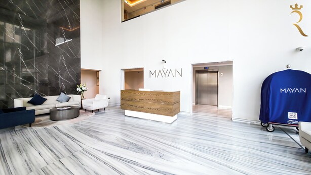 A modern reception area with a marble floor, a reception desk, a blue waiting area, and an elevator. - Mayan Building Apartments by RHH (Abu Dhabi)