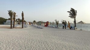 A beach with rows of sun loungers, palm trees, and a calm sea. - Mayan Building Apartments by RHH (Abu Dhabi)