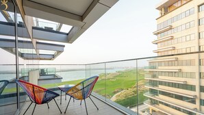 A balcony with a view of a golf course and a body of water, featuring modern chairs and a glass railing. - Mayan Building Apartments by RHH (Abu Dhabi)