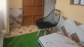 A room with a green artificial turf floor, a white marble table, a black chair, a wooden door, and a window with a view.